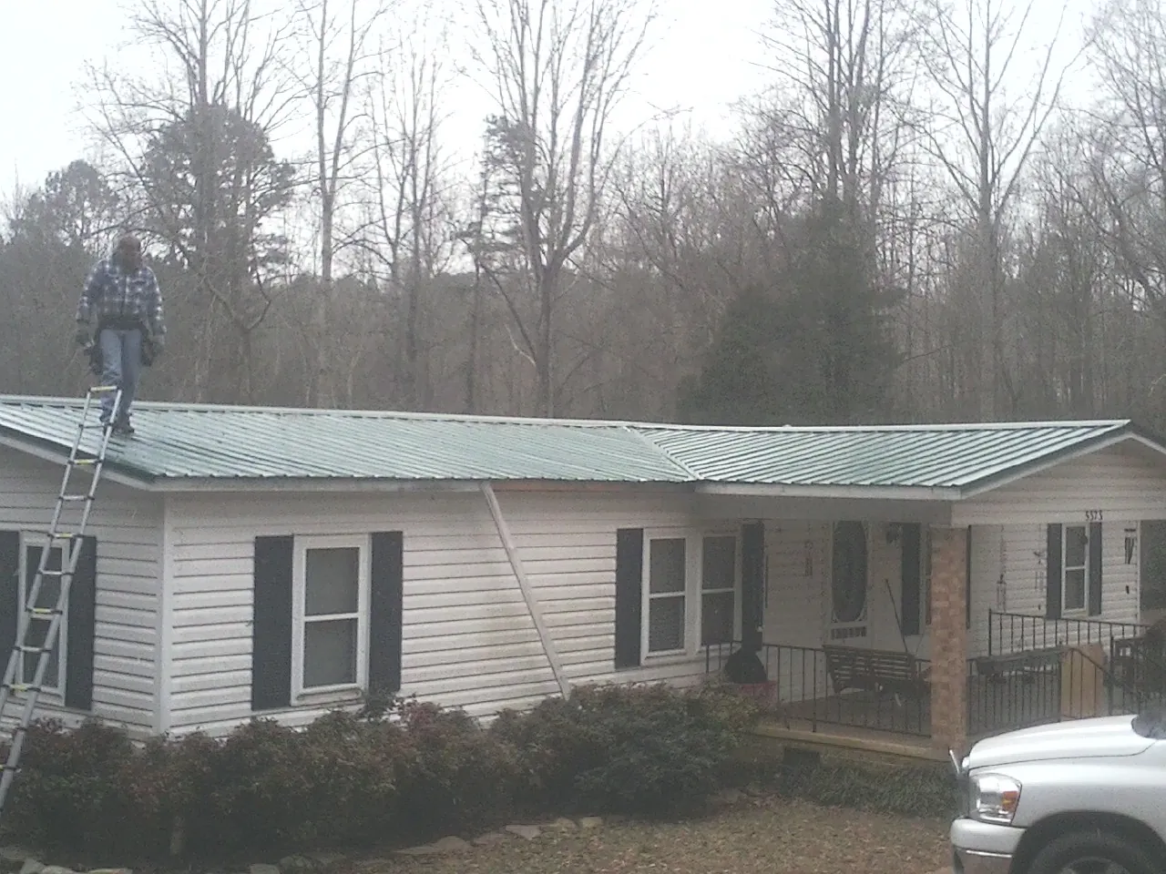 Worker on a ladder beside a new green metal roof on a ranch home in Jonesborough