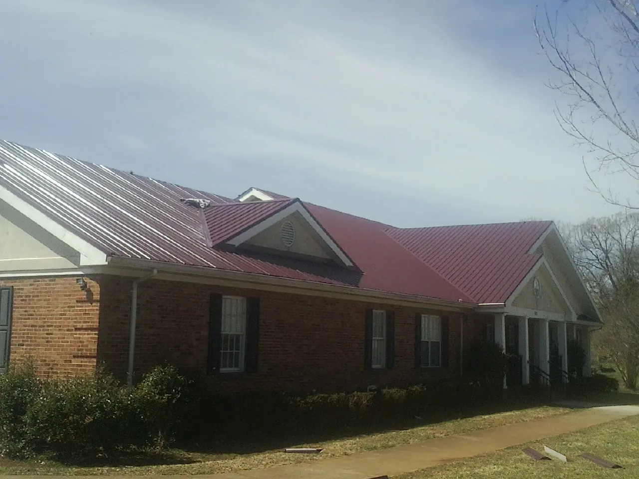 Red metal roof with gabled entries on a long brick building, from a Hail Damage Roof Repair job in Jonesborough