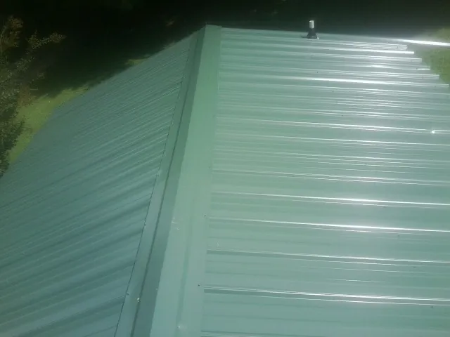New green metal panels meeting at the ridge of a roof — Flat Roof Repair work by our crew in Jonesborough