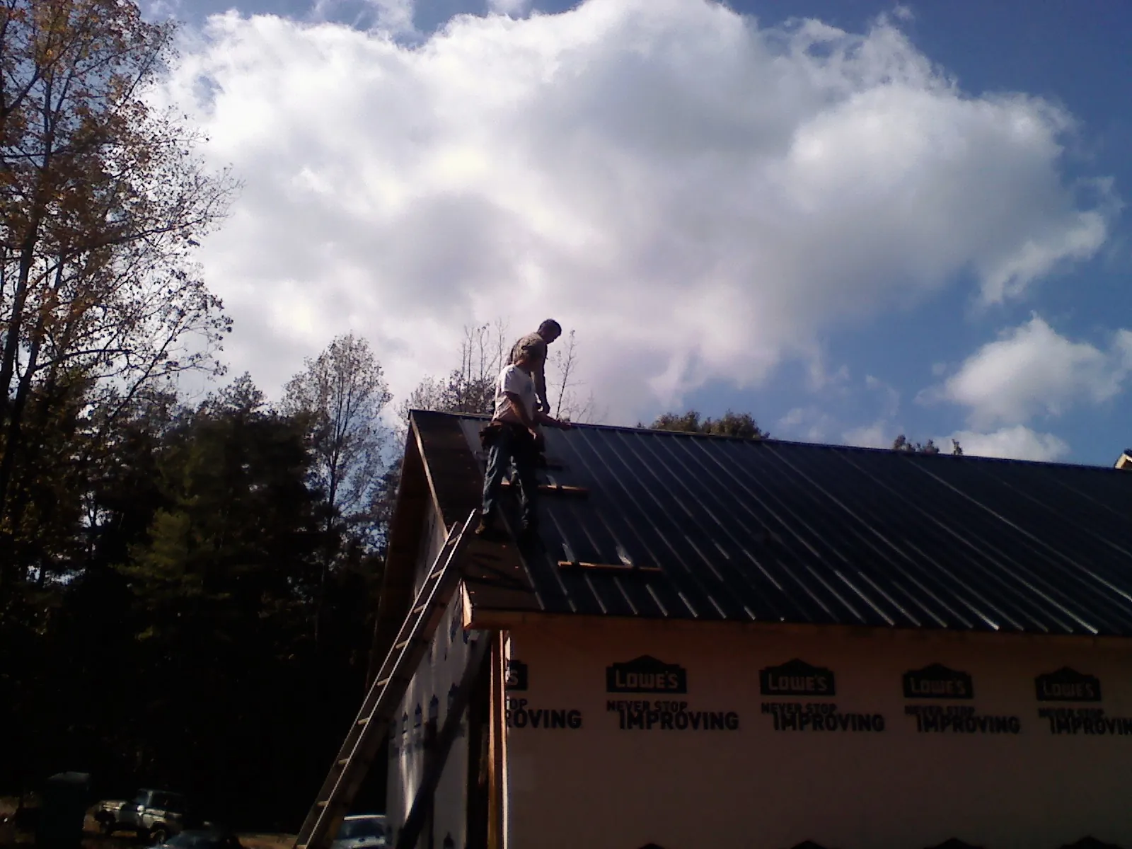 Roofer fastening dark metal panels high against a cloudy sky, from a Roof Inspection job in Jonesborough