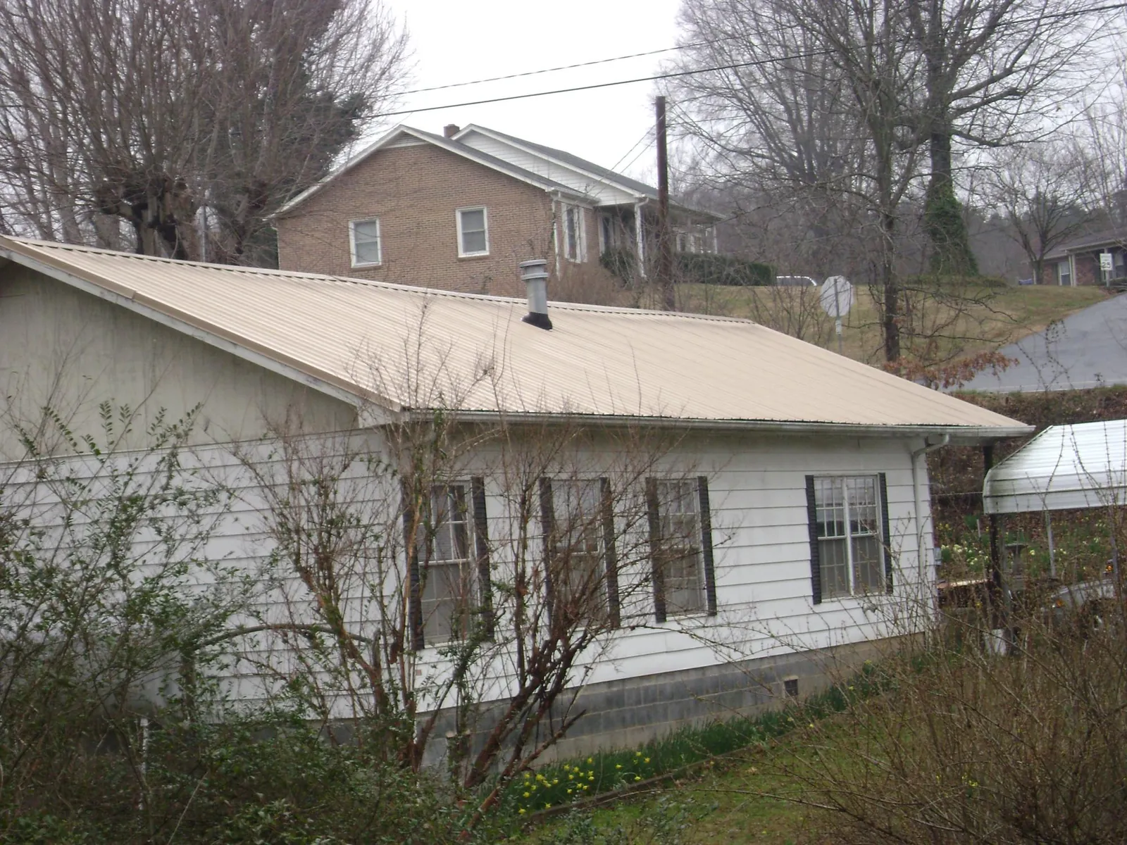 Tan metal roof on a white sided house set into a hillside — Commercial Roofing by Roofing Brothers in Jonesborough
