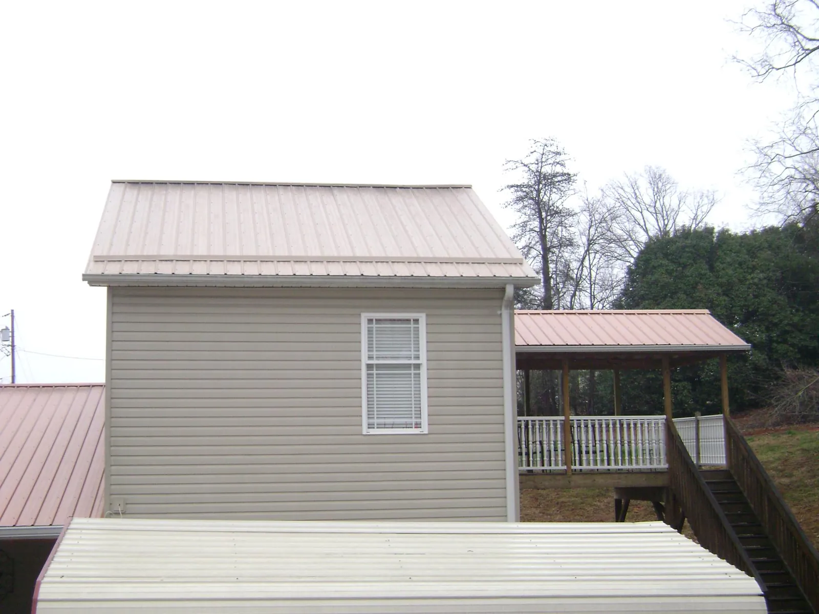 Tan metal roofs on a two story addition and attached porch, from a Roof Replacement job in Jonesborough